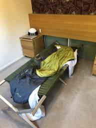 Army green camping bed in a bedroom, with sleeping bag